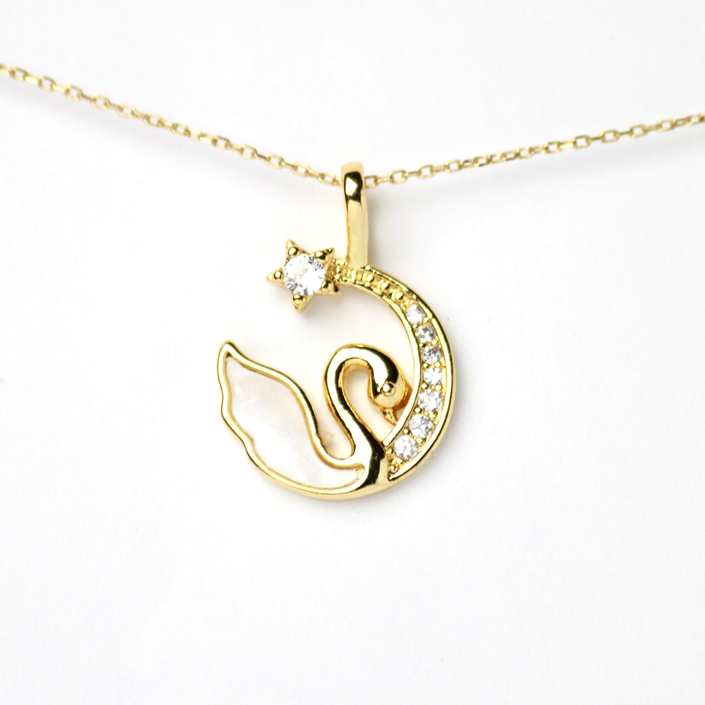 Dije de cisne, su cuerpo esta hecho de madreperla mientras que la media luna mantiene incrustaciones de Zirconias y un Diamante en la punta en forma de estrella, Oro laminado