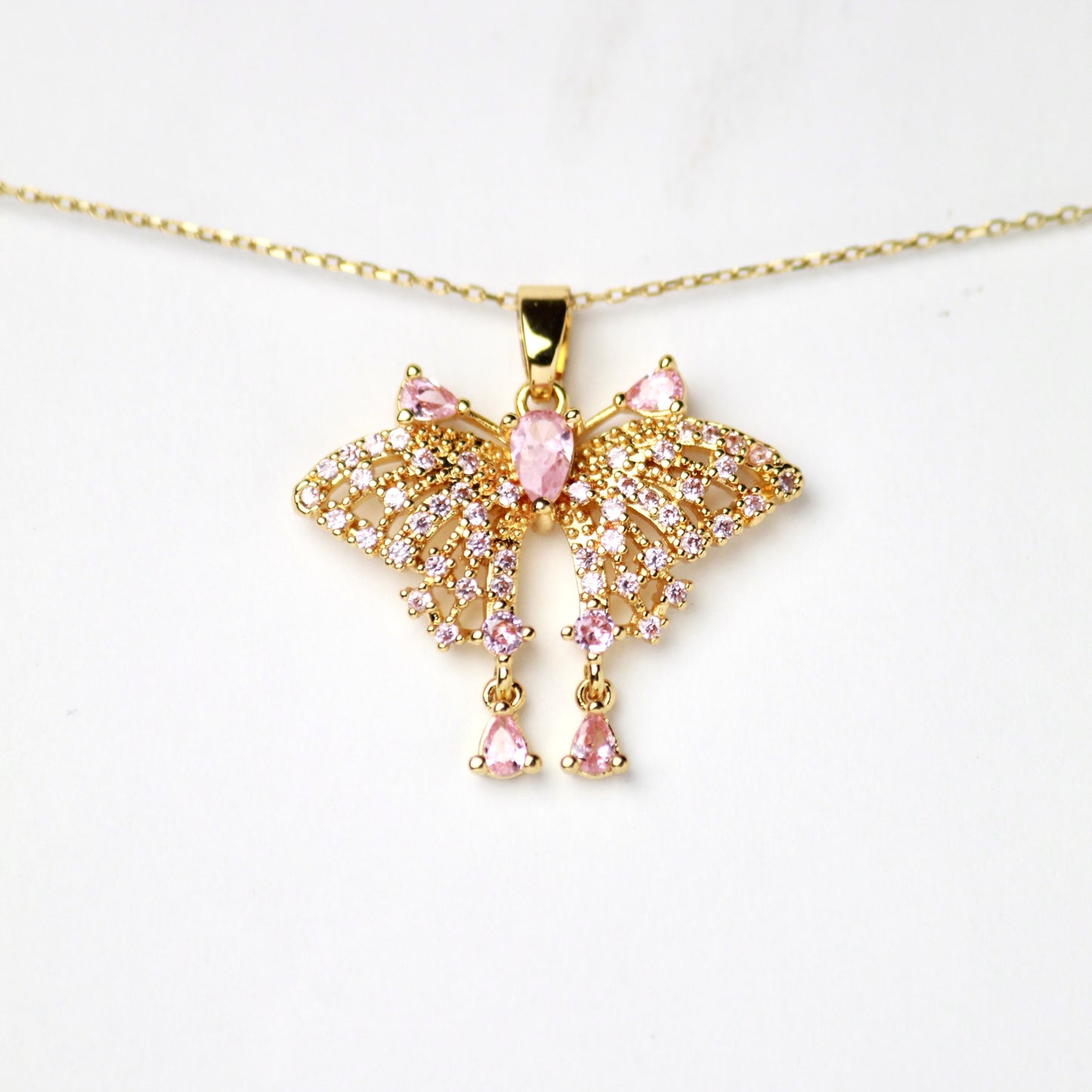 Dije de Mariposa con Diamante central en Corte pera color Rosado, incrustaciones de Zirconias rosadas en sus alas y Diamantes brillantes en Corte pera flotantes, Oro laminado