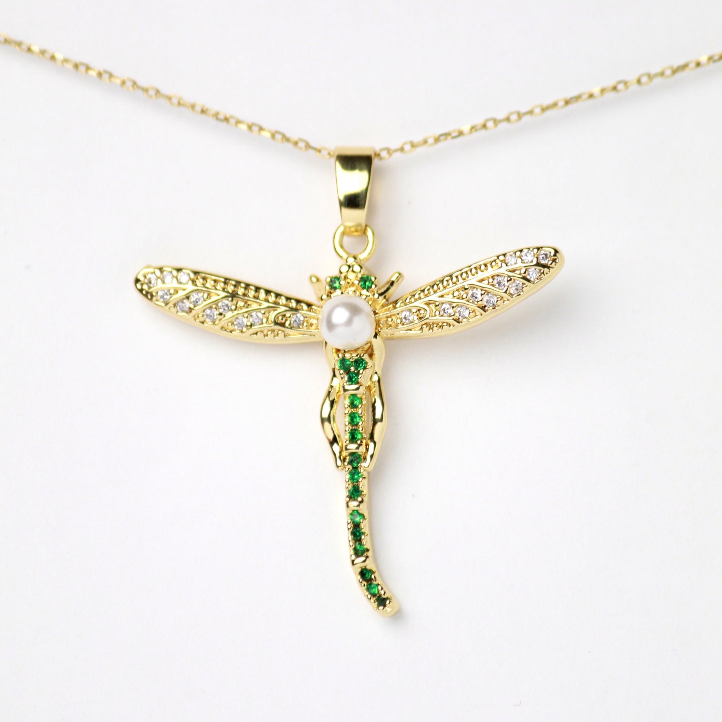 Este dije de libélula combina alas brillantes con Diamantes incrustados y una perla central, a su cuerpo lo adornan Zirconias color verde Esmeralda. Oro laminado