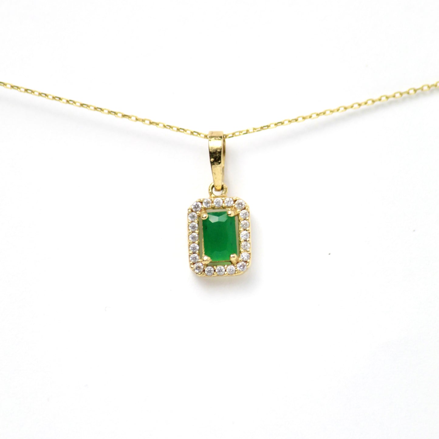 Dije de Oro 10k, rectangular con piedra central verde estilo esmeralda, rodeada de un marco brillante de zirconias que aportan luz y sofisticación